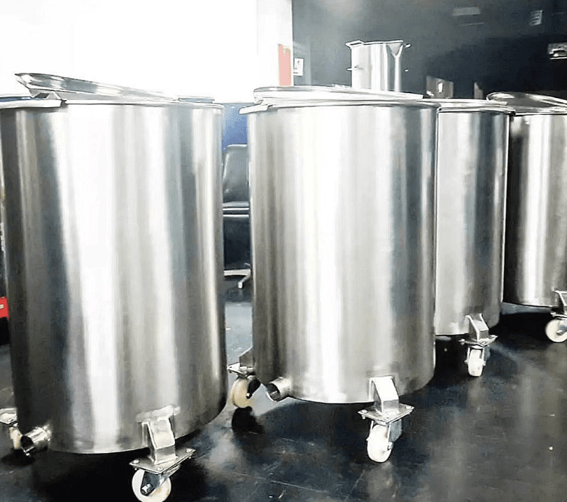 Tanques cilíndricos de acero inoxidable con tapas y ruedas alineados en un entorno industrial.