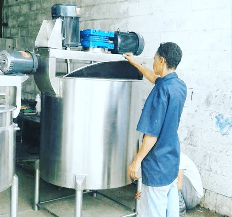 Hombre con camisa azul inspeccionando un gran tanque industrial de acero inoxidable con motores.