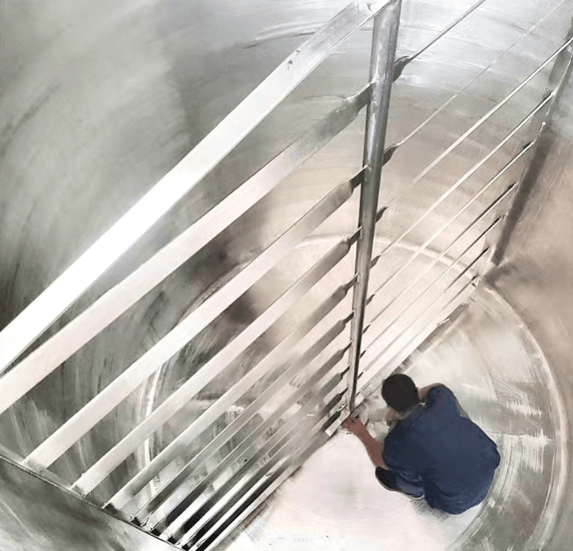 Operario inspeccionando el interior de un gran tanque industrial de acero inoxidable con aspas mezcladoras.