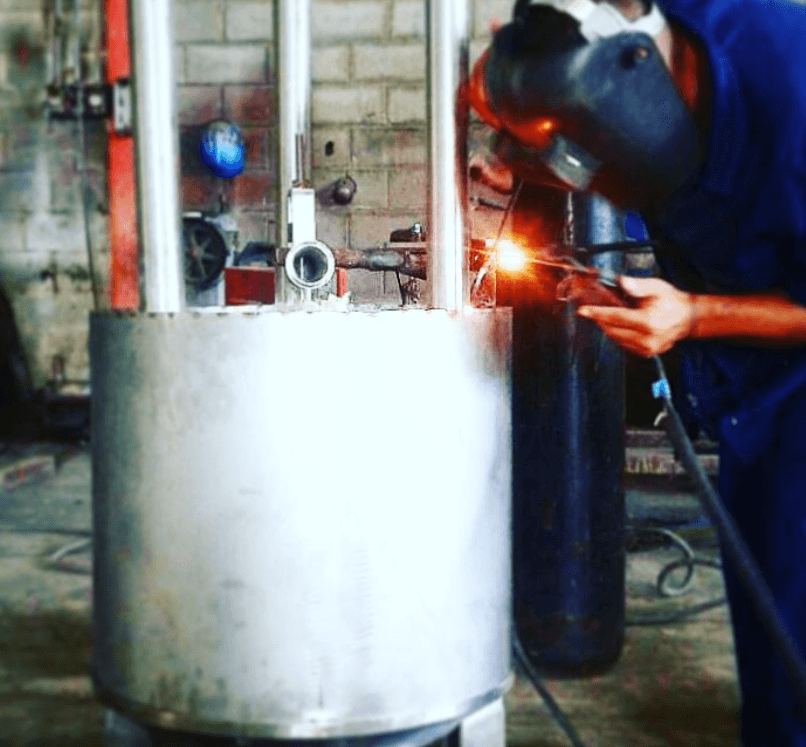 Soldador con casco protector une piezas de un cilindro metálico grande generando chispas brillantes.