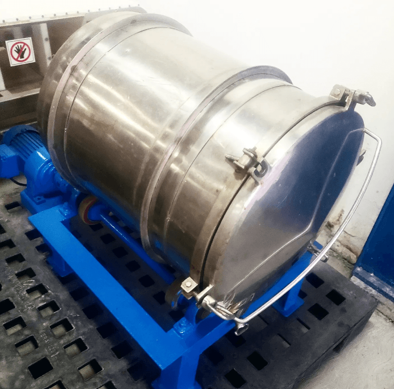 Tambor cilíndrico de acero inoxidable sobre soporte azul con motor eléctrico en un palé.