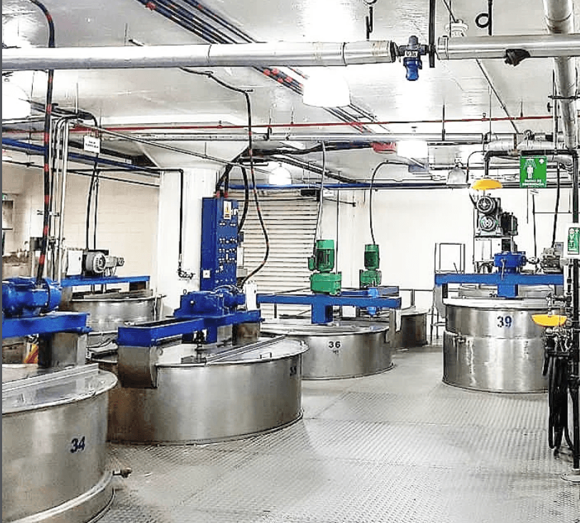 Grandes tanques de acero inoxidable numerados en una fábrica con tuberías y maquinaria industrial azul.