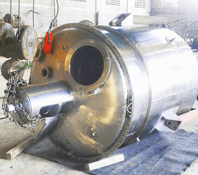 Tanque industrial de acero inoxidable con abertura circular y cadenas dentro de un taller.