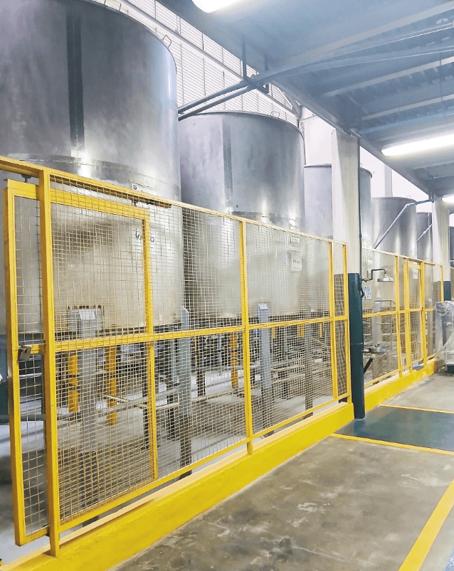 Grandes tanques industriales de acero inoxidable detrás de una valla de seguridad amarilla.
